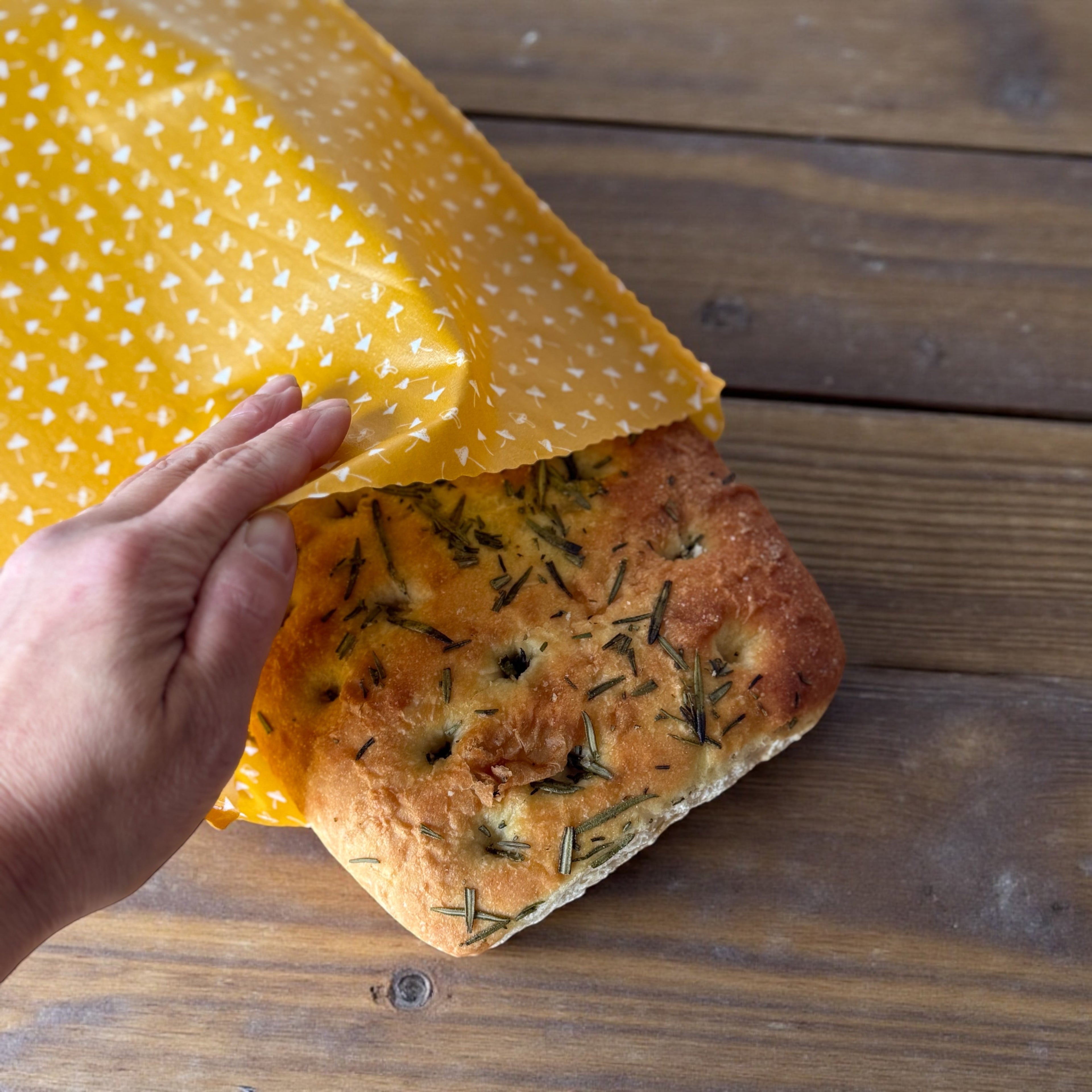 Hand holding a loaf of bread wrapped in yellow beeswax wrap on a wooden surface